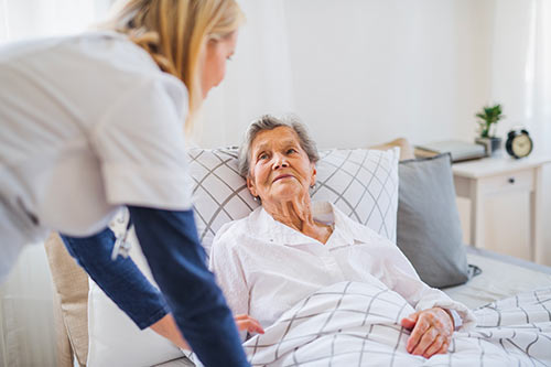 Image d'une personne âgée sur un lit médicalisé en location avec son aide soignante
